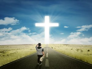 picture showing a man holding a guitar looking at the cross in the end of the road