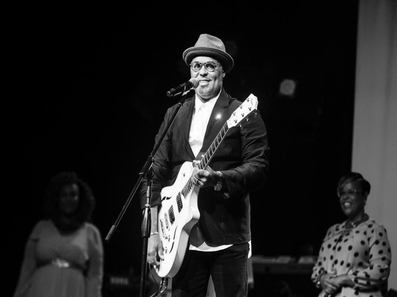 Contemporary Christian Musician Israel Houghton plays guitar and sings on stage with 2 women standing in the background
