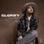 Jordan Feliz wearing a fatigue jacket sitting while looking upwards, cover art for his song "Glorify" - My Christian Musician