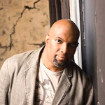 Lamar Campbell staring at the camera while leaning on a wall - My Christian Musician