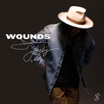 Jordan Feliz looking downwards, and an overlay showing his signature and the text "WOUNDS" - My Christian Musician
